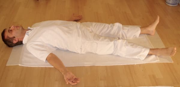Man lying flat on his back with arms and legs relaxed in Corpse Pose